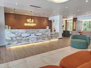 Un hall d’accueil d’hôtel avec un comptoir de réception en marbre, des panneaux muraux en bois et un éclairage moderne.