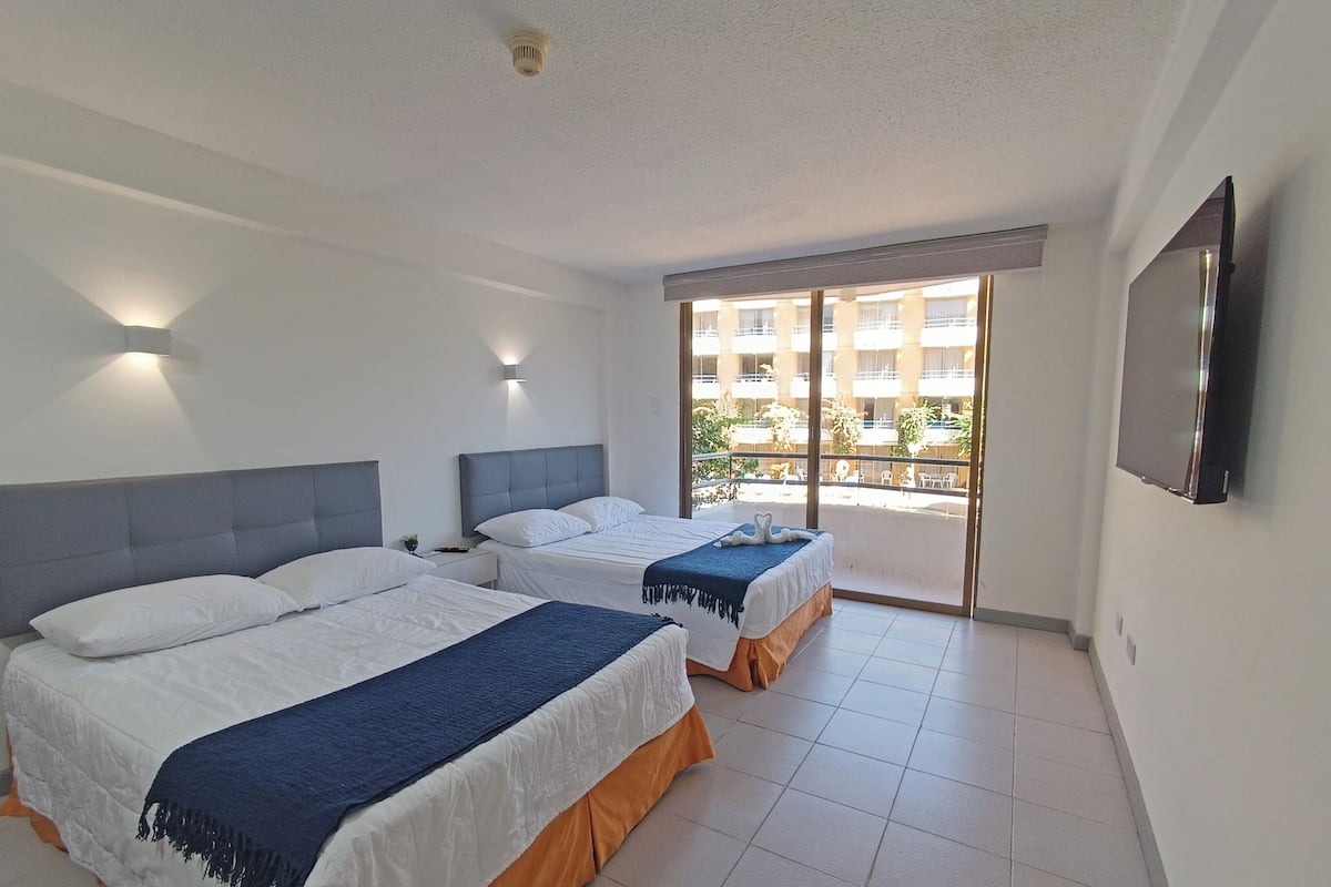 A hotel room with two beds, a balcony with a view, and a TV mounted on the wall.