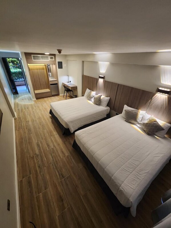 Een hotelkamer met twee bedden, een bureau en een kleine kitchenette.