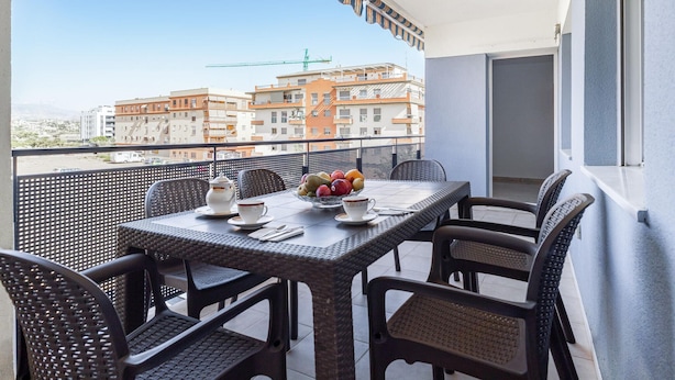 A balcony with a table set for two, featuring wicker chairs and a bowl of fruit.