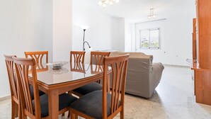 A modern living room with a dining table, four wooden chairs, a sofa, and a wooden cabinet.