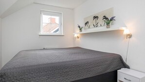 Ein Schlafzimmer mit einem großen Bett, einem kleinen Nachttisch, einem Fenster und einem Wandregal mit Pflanzen.