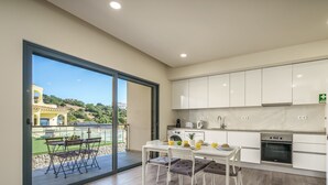 Una cocina moderna con armarios blancos, un comedor con mesa y sillas, y un amplio ventanal corredero que da a un patio exterior.