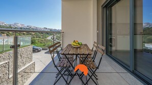 Un balcón con mesa y sillas, un cuenco de fruta y vistas a un paisaje urbano.