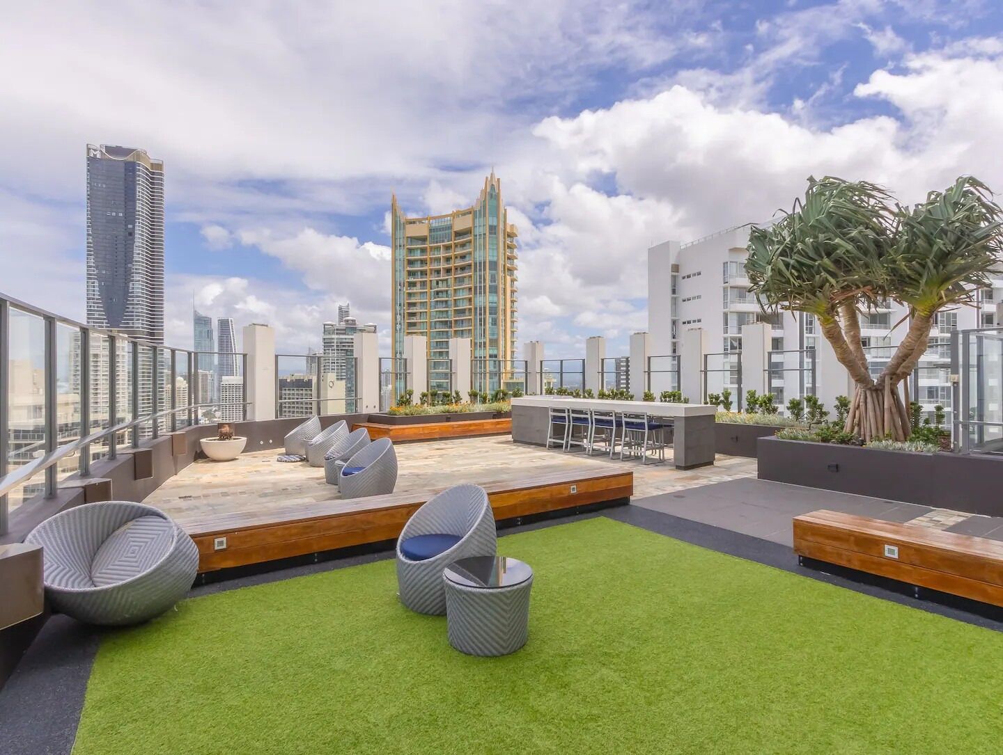 Terraço no telhado com grama sintética verde, mobiliário moderno e vista para edifícios ao redor.