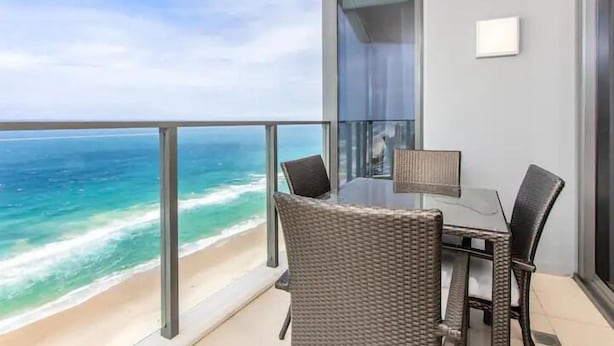Un balcon avec vue sur l’océan, une porte vitrée et une table avec des chaises.