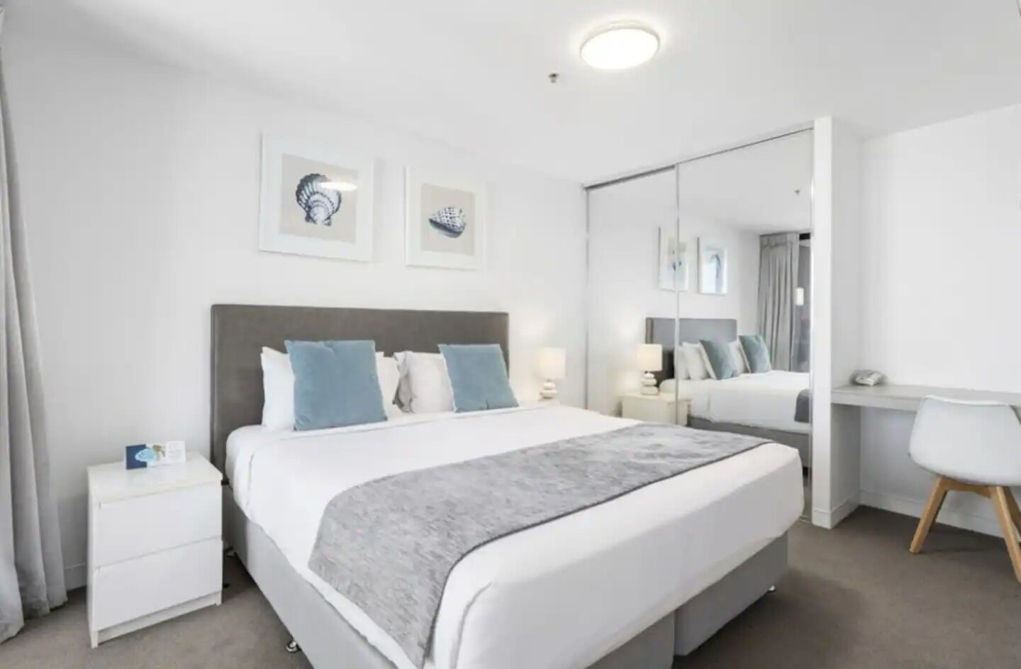 A modern hotel room with a large bed, bedside tables, a desk, and a mirror.