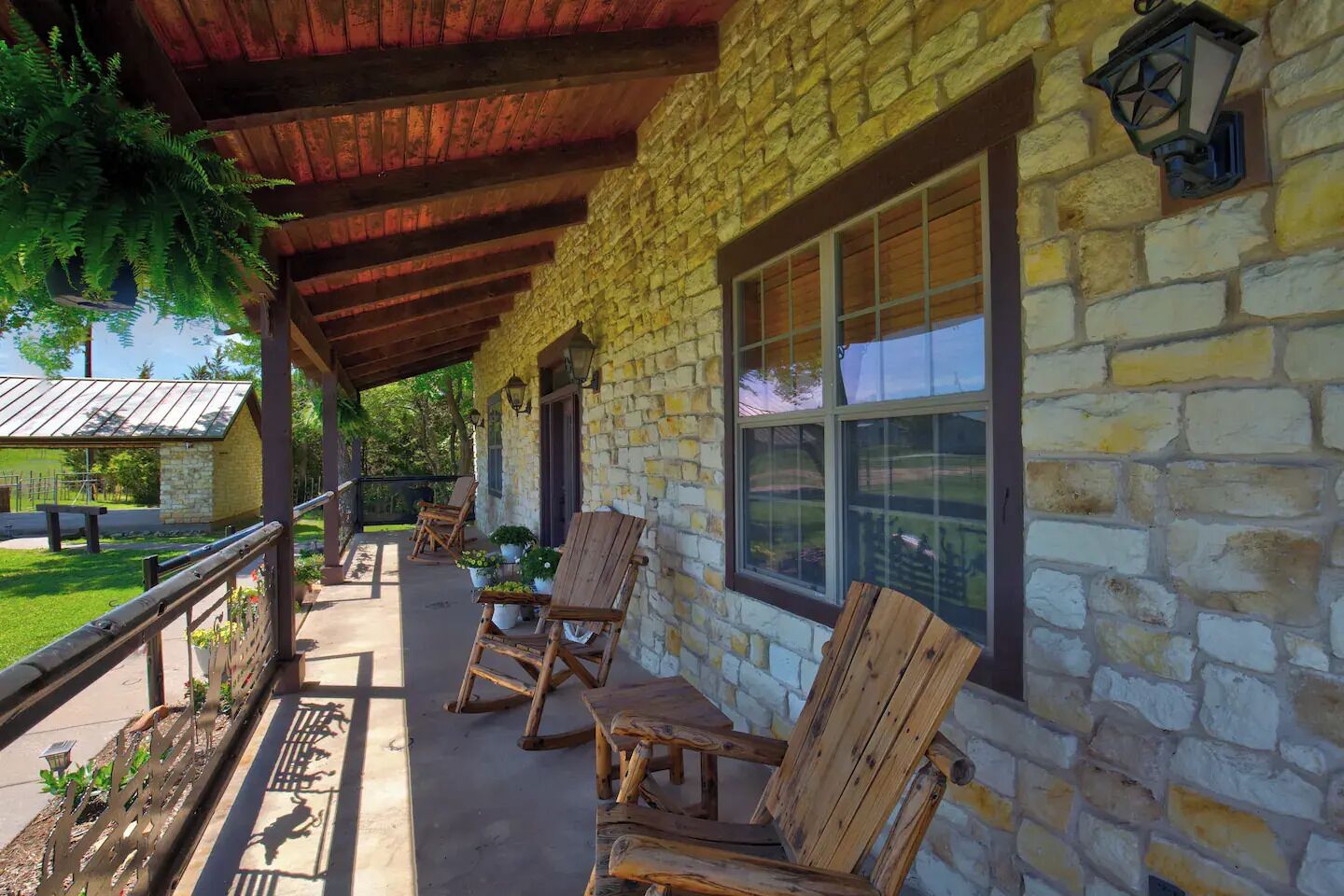 A covered porch with stone walls, wooden chairs, and potted plants.