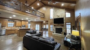A spacious living area with a fireplace, leather sofas, and a kitchen in the background. - Peaceful Texas Ranch Retreat on the Lake (Midlothian)