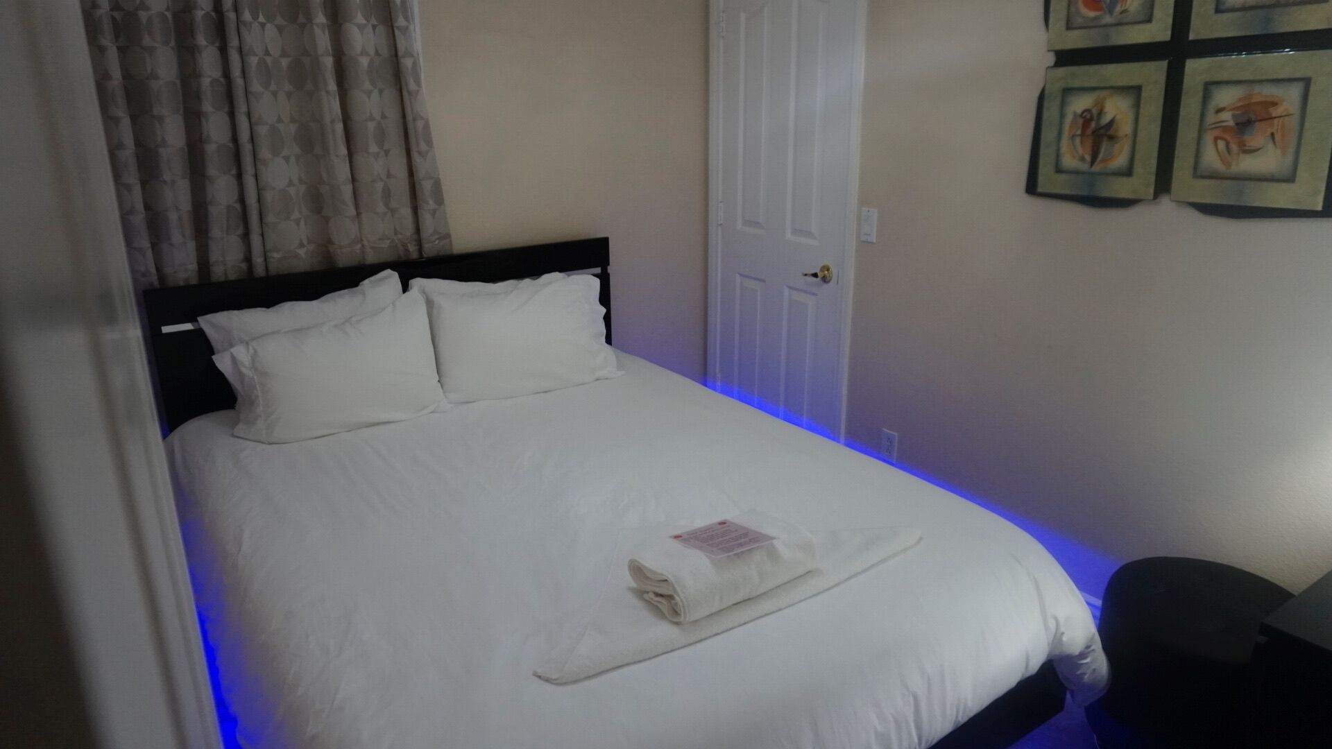 Un lit bien fait, avec du linge de lit blanc et des oreillers, une serviette pliée posée sur le lit, et une porte dont la poignée se trouve à droite.