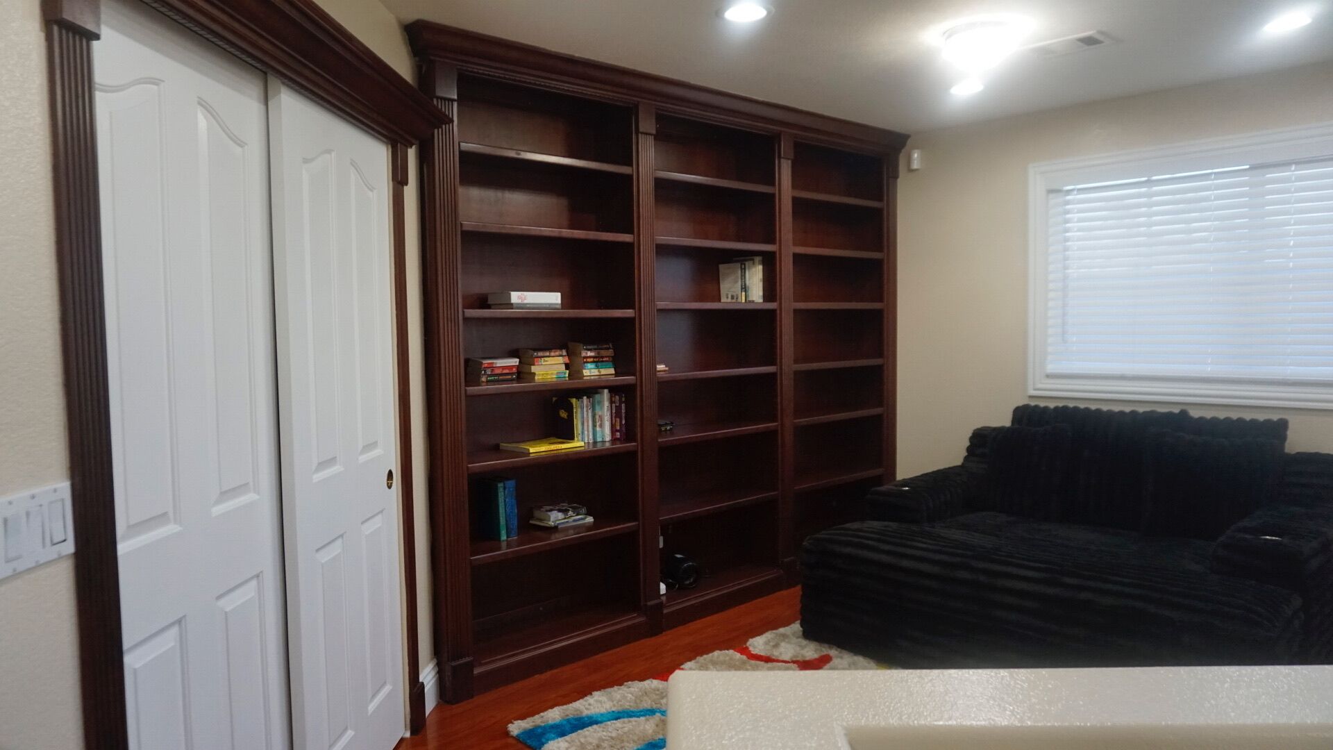A living room with a dark-colored sofa, a wooden bookshelf, and a white door.