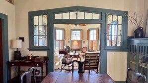 A dining room with a wooden table, chairs, and a view into the kitchen through a bay window.