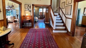 A spacious hallway with a wooden staircase, a chandelier, and a red patterned rug.
