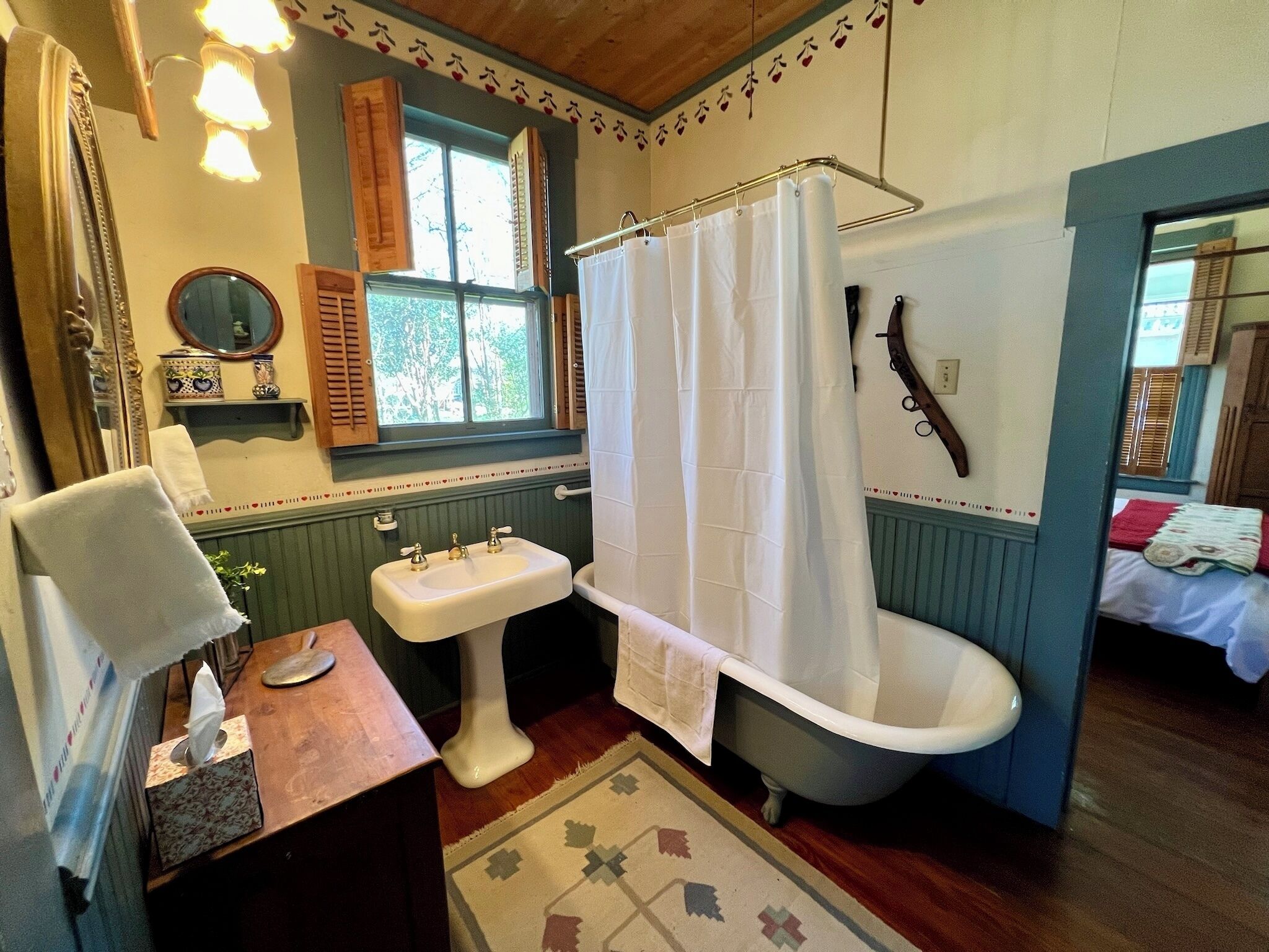 A bathroom with a clawfoot bathtub, a pedestal sink, and a window with shutters.