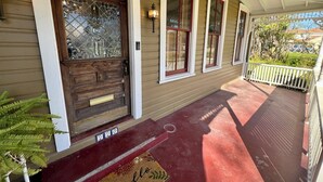 A wooden front door with a glass panel, a porch with a red floor, and a white railing.