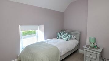 Un dormitorio con una cama, una mesita de noche, una lámpara y una ventana.