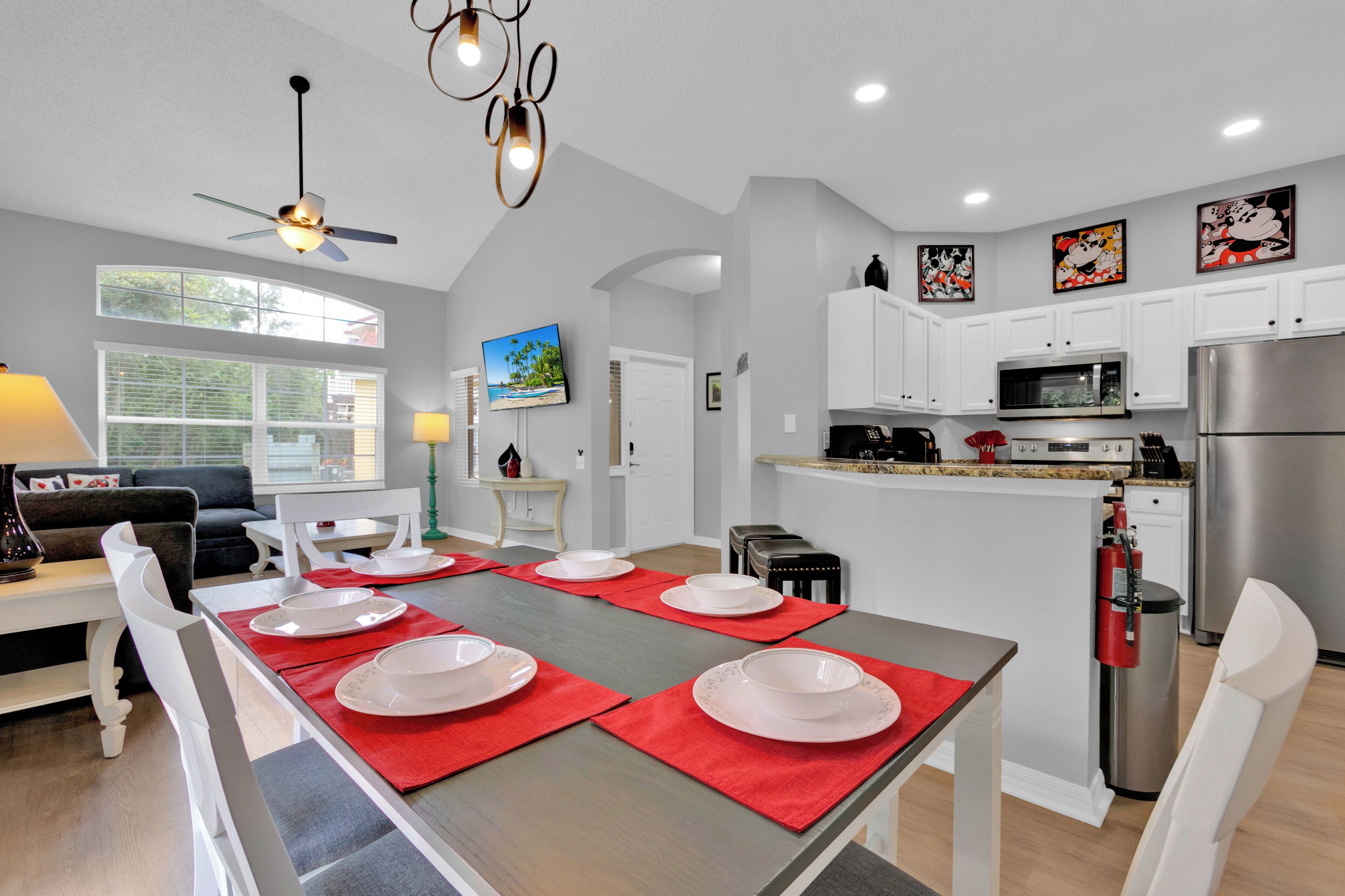 A modern kitchen with white cabinets, a stainless steel refrigerator, and a dining area set with red placemats and white plates.