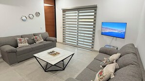 A living room with a grey sofa, a coffee table, a ceiling fan, a TV, and a window with blinds. - “Your Perfect Getaway: Brand-New Condo in Cabo San Lucas” (Cabo San Lucas)