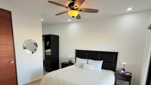 A bedroom with a bed, a ceiling fan, a nightstand, a mirror, and a wardrobe. - “Your Perfect Getaway: Brand-New Condo in Cabo San Lucas” (Cabo San Lucas)
