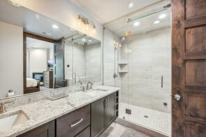 Een moderne badkamer met een grote spiegel, twee wasbakken, een douche en een douchecabine met glazen wanden.