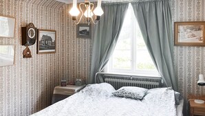 A bedroom with a bed, a dresser, a nightstand, a clock, and a window with curtains.