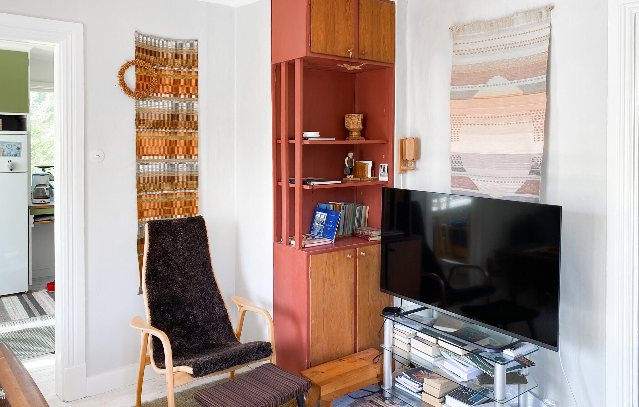 Uma sala de estar com televisão, estante de livros, cadeira e um armário vermelho.