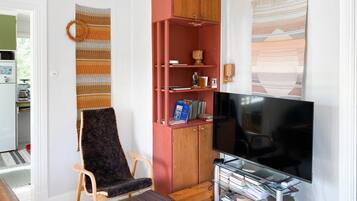Uma sala de estar com televisão, estante de livros, cadeira e um armário vermelho.