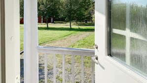 A view through a door with a white frame and a glass window, leading to a grassy yard with trees and a red building in the background.