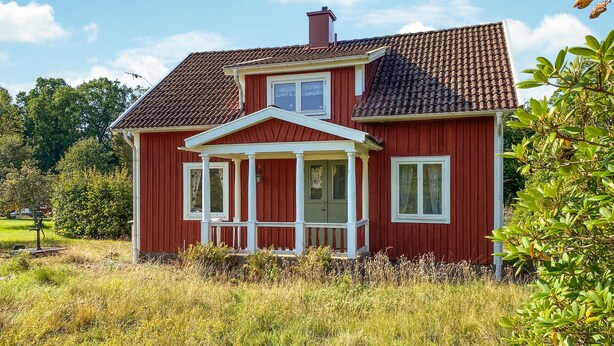 A red house with a white porch, a chimney, and a tiled roof.