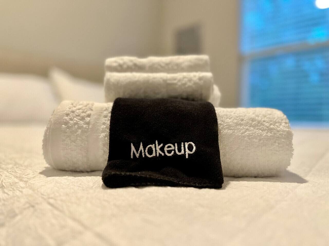 Une serviette blanche, soigneusement pliée, et une serviette noire portant l’inscription « Maquillage » se trouvent dans une chambre d’hôtel.