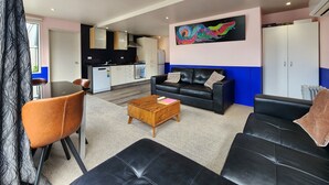 A modern living room with a black leather sofa, a wooden coffee table, and a dining area with a brown leather chair.