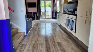 A modern kitchen with wooden flooring, white cabinets, and a sliding glass door leading to a balcony.