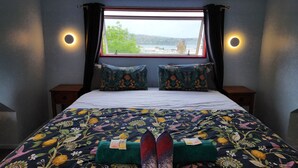 A bed with floral bedding, two pillows, and a view of a landscape through a window.