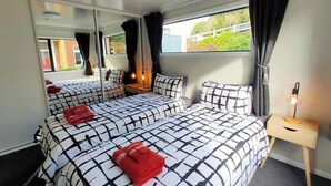 Un dormitorio con dos camas, un espejo, una mesita de noche con lámpara y una ventana con cortinas.