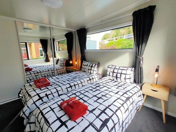 Une chambre avec deux lits, un miroir, une table de chevet avec une lampe et une fenêtre avec des rideaux.