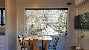 Un comedor con una mesa y sillas, una ventana con persianas y un televisor montado en la pared.