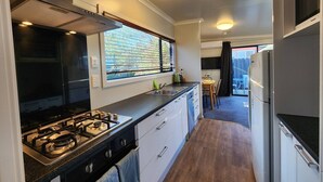 Una cocina compacta con estufa a gas, armarios blancos y una ventana con persianas.