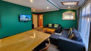 Una habitación con una mesa de madera, un sofá azul oscuro y un televisor en la pared.