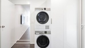 Une buanderie équipée de deux machines à laver et de deux sèche-linge à chargement frontal superposés, un escalier menant à une autre pièce et un tableau encadré accroché au mur.