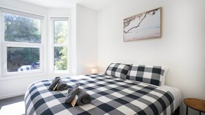 Une chambre avec une couvre-lit à carreaux, deux oreillers, une table de chevet et un tableau accroché au mur.