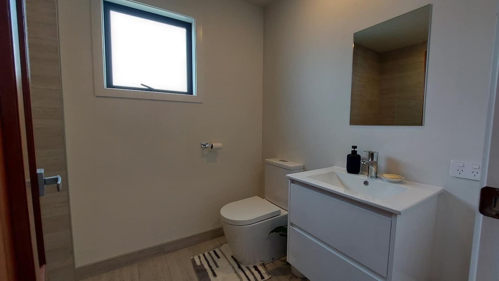 A small, clean bathroom with a toilet, sink, and window.