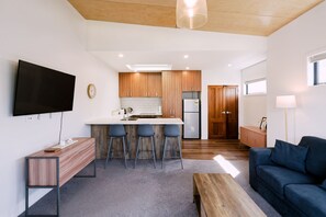 A modern kitchen with wooden cabinets, a central island with bar stools, a built-in TV, and a large window.