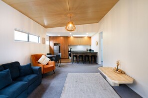 Ein modernes Wohnzimmer mit einer Couch, einem Essbereich mit Stühlen, einer Küche mit Holzschränken und einer Hängeleuchte.
