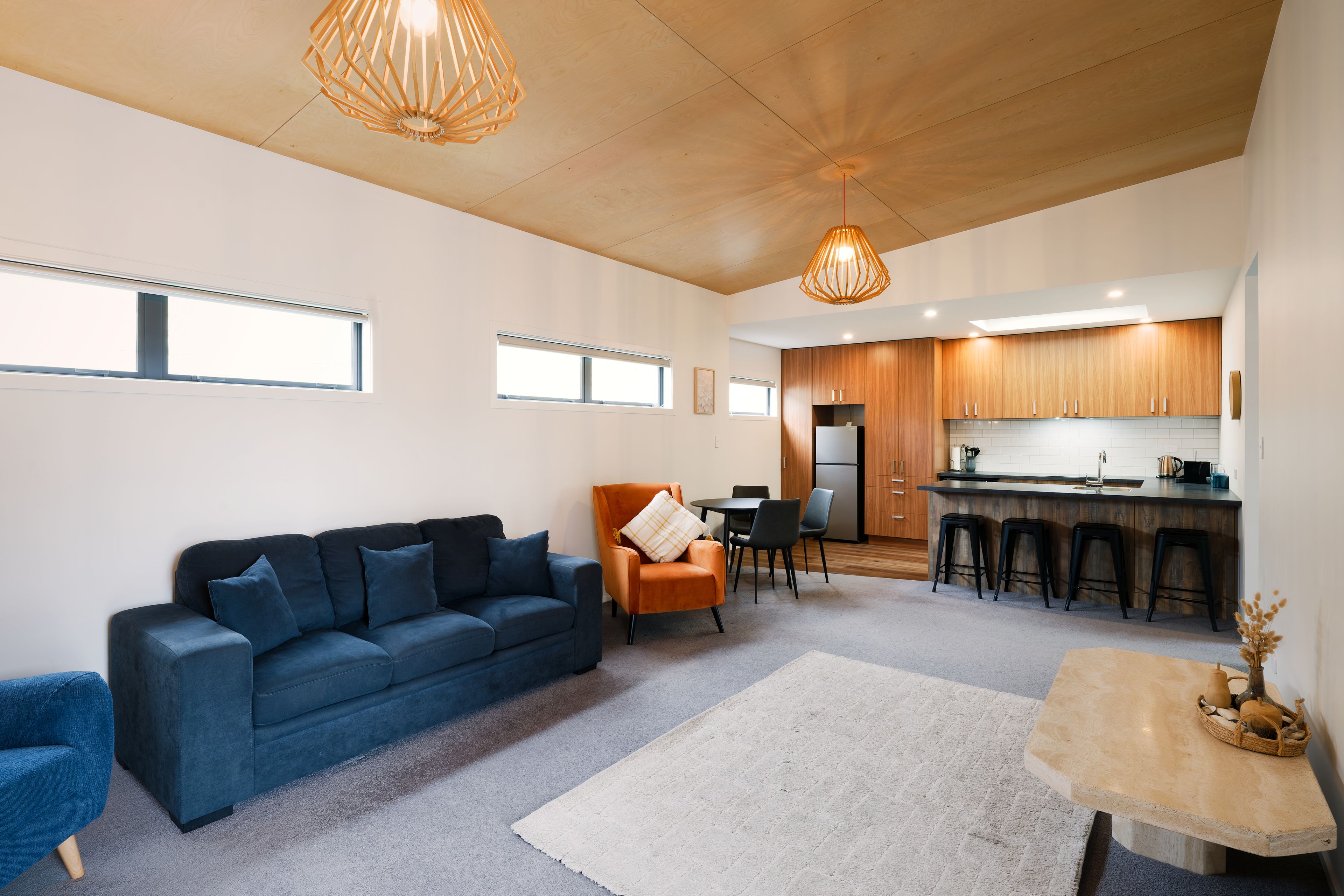 A modern living room with a blue sofa, a small orange armchair, and a white rug.