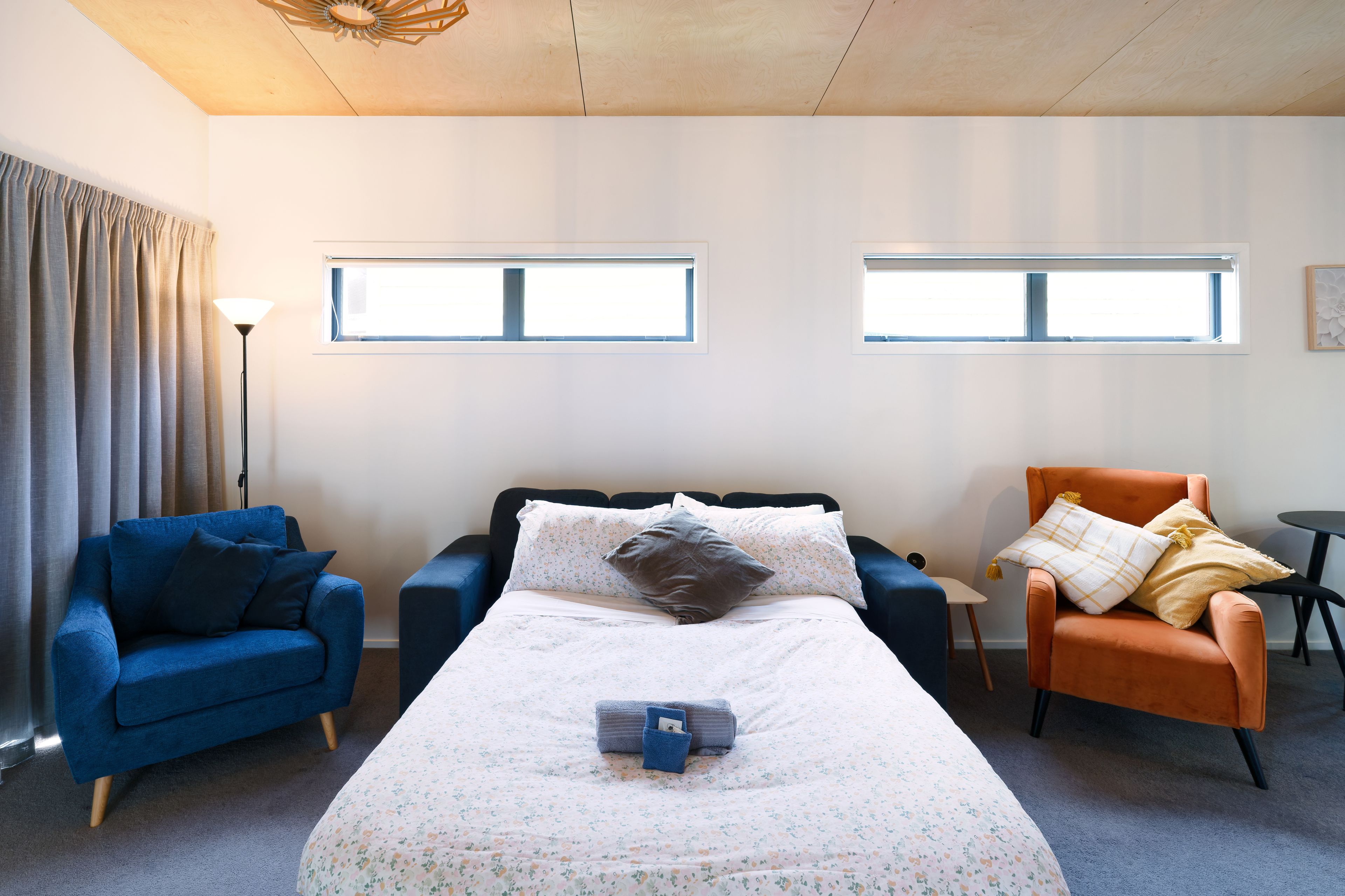 A hotel room with a bed, two sofas, a chair, and two windows.
