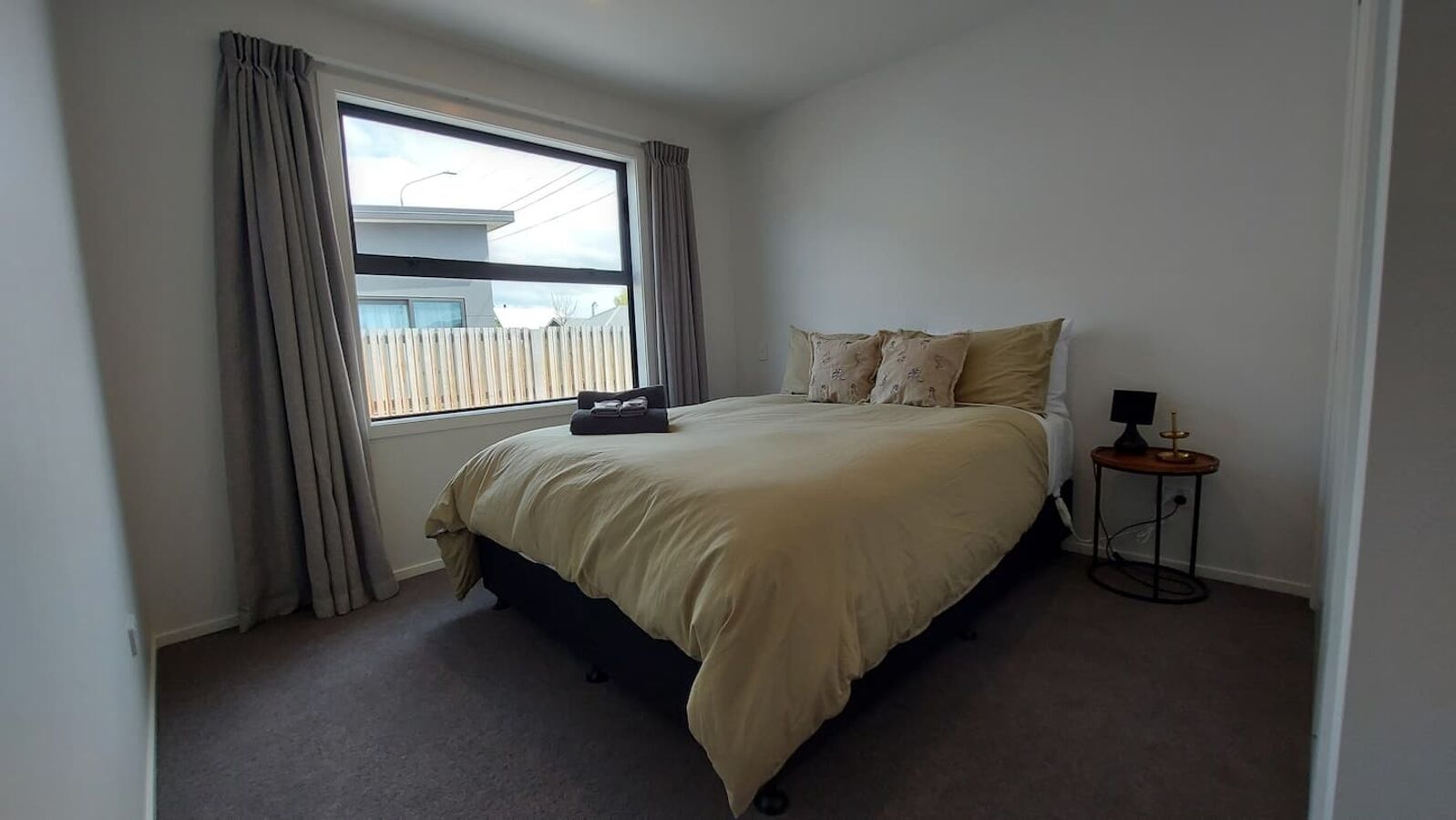 Une chambre à coucher avec un lit, une fenêtre avec des rideaux, une table de chevet avec une lampe et un radiateur.