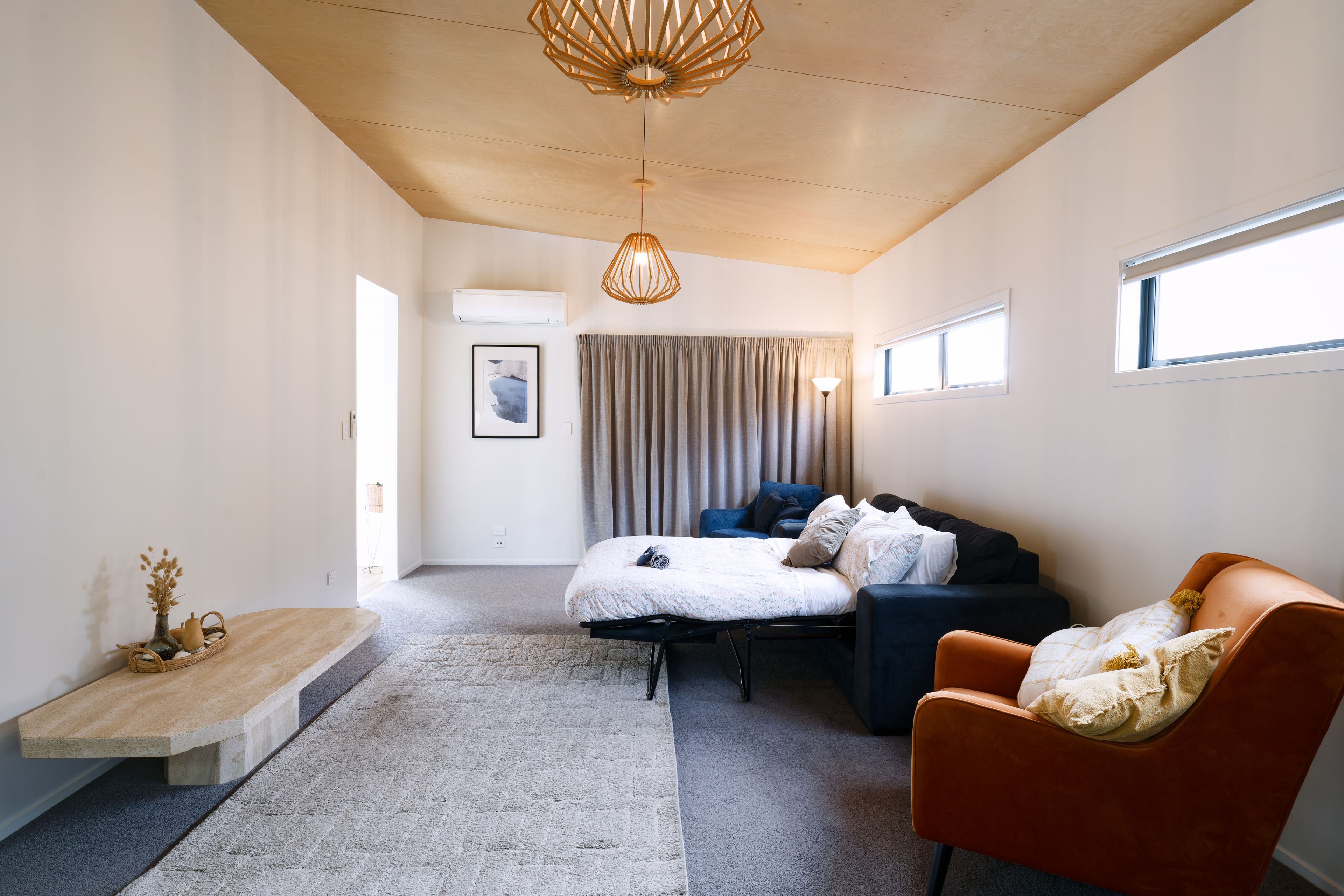 A modern bedroom with a bed, a sofa, a chair, a bedside table, and a window.