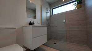 A modern bathroom with a walk-in shower, a toilet, and a vanity with a mirror. - Sleek Suite by the Sand (2-bedroom) (Dunedin)