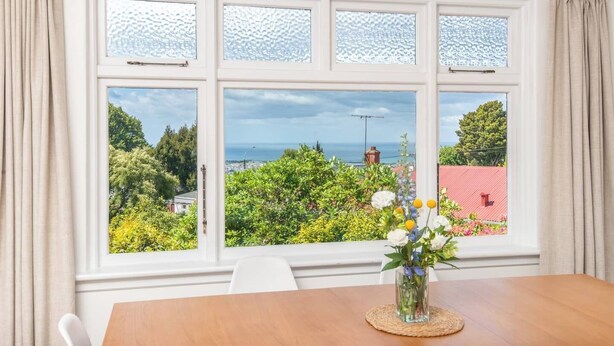 A dining area with a view of a garden and sea through a large window with multiple panes.