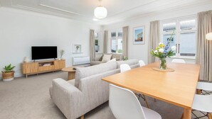 A modern living room with a sofa set, a wooden dining table, and a flat-screen TV.
